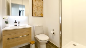 A bathroom with a white sink, wooden vanity, a toilet, and a shower area. - Honeycomb (Auckland)