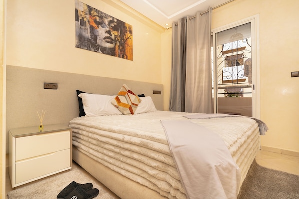 Een net opgemaakt bed met een zachte witte dekbed, een nachtkastje met een lamp en een schilderij aan de muur.