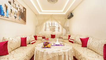 A room with a sofa set, a table with a vase and fruit, and a painting on the wall.
