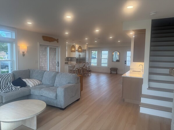 A spacious living area with a grey sofa, a round coffee table, and a kitchen in the background. - Direct Ocean Front 3-bedroom custom, new construction house (Hull)