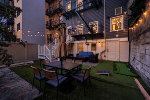 Ein Garten mit Terrassentisch, Stühlen, einer blauen Couch und einem kleinen Putting-Green.