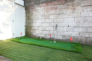A miniature golf course with three holes, each marked by a red flag, against a concrete wall. - Classic 3 bedroom Hoboken Retreat  Private Backyard (Hoboken)