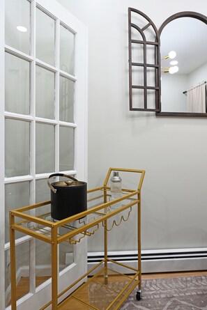 Ein Zimmer mit einer weißen Tür, einem Spiegel und einem Metallrollwagen mit einem schwarzen Topf und einer Glasflasche.