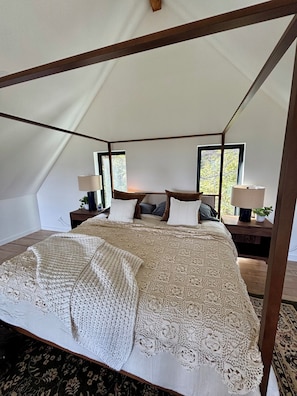 A tent-style bedroom with a four-poster bed, two bedside tables with lamps, and a view of trees through the windows. - Timber&Tonic Mountain Chalet—2 min to beach (Sagle)