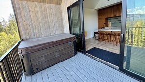 En balkon med jacuzzi, træterrasse og udsigt til et køkkenområde med barstole.