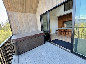 A balcony with a hot tub, wooden deck, and a view of a kitchen area with bar stools. - Timber&Tonic Mountain Chalet—2 min to beach (Sagle)