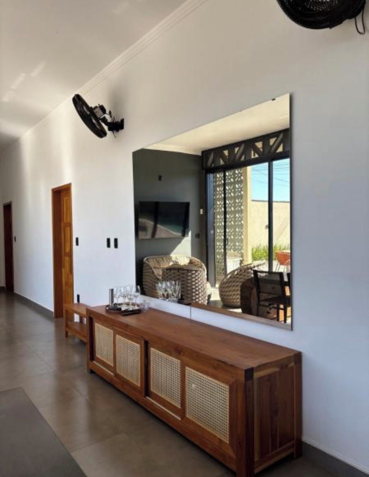 A modern interior with a long wooden console table, a large mirror reflecting the room, and a ceiling fan.