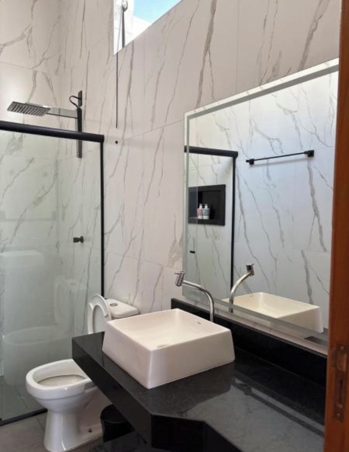 Ein modernes Badezimmer mit einer Duschkabine aus Glas, einer weißen Toilette und einer schwarzen Ablagefläche mit einem weißen Waschbecken.