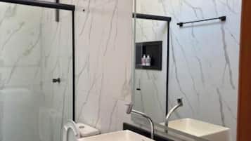 Ein modernes Badezimmer mit einer Duschkabine aus Glas, einer weißen Toilette und einer schwarzen Ablagefläche mit einem weißen Waschbecken.