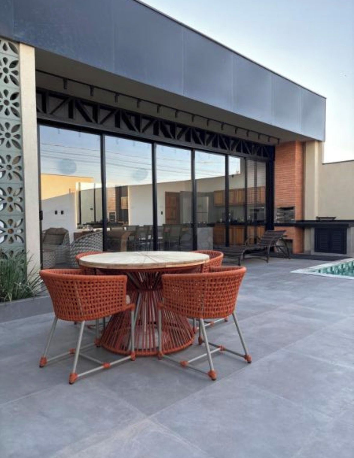 Une terrasse extérieure moderne avec une table ronde et des chaises orange, une piscine et un bâtiment doté de grandes fenêtres et d’une façade décorative.