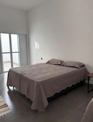 Quarto com cama, mesa de cabeceira e vista pela janela.