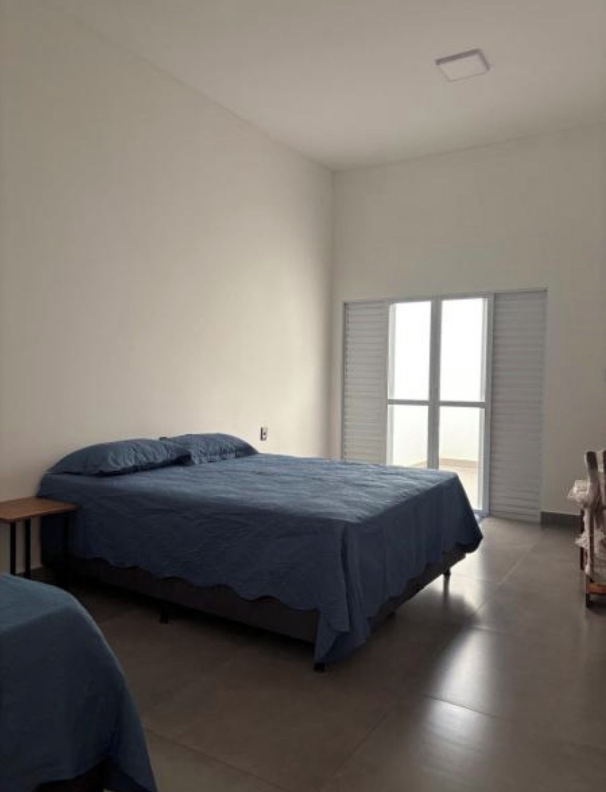Un dormitorio con cama, una mesita, una silla y una ventana con persianas.