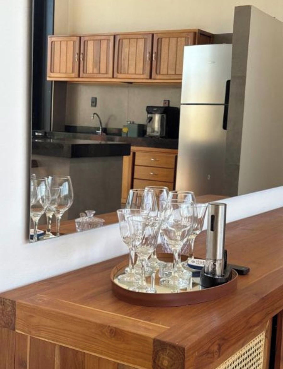 A kitchen with wooden cabinets, a stainless steel refrigerator, and a wooden counter with a tray holding wine glasses and a bottle.