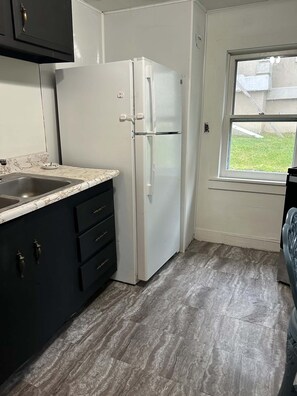 A compact kitchen with a white refrigerator, dark cabinetry, a marble countertop, and a window with a view of the outdoors.