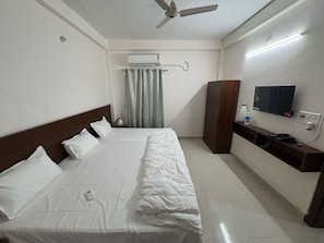 Una habitación de hotel con cama, armario, televisor y ventilador de techo.