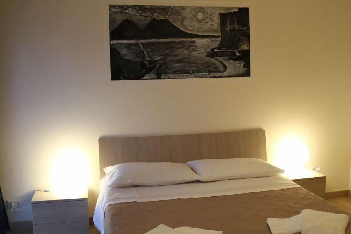 Une chambre à coucher avec un lit, deux tables de chevet et un tableau accroché au mur.
