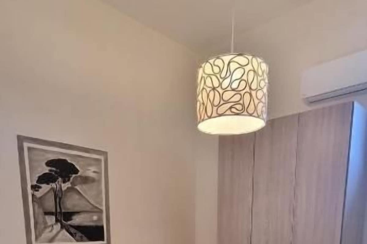 Un lit bien fait, avec une tête de lit, un luminaire suspendu et un tableau encadré accroché au mur.