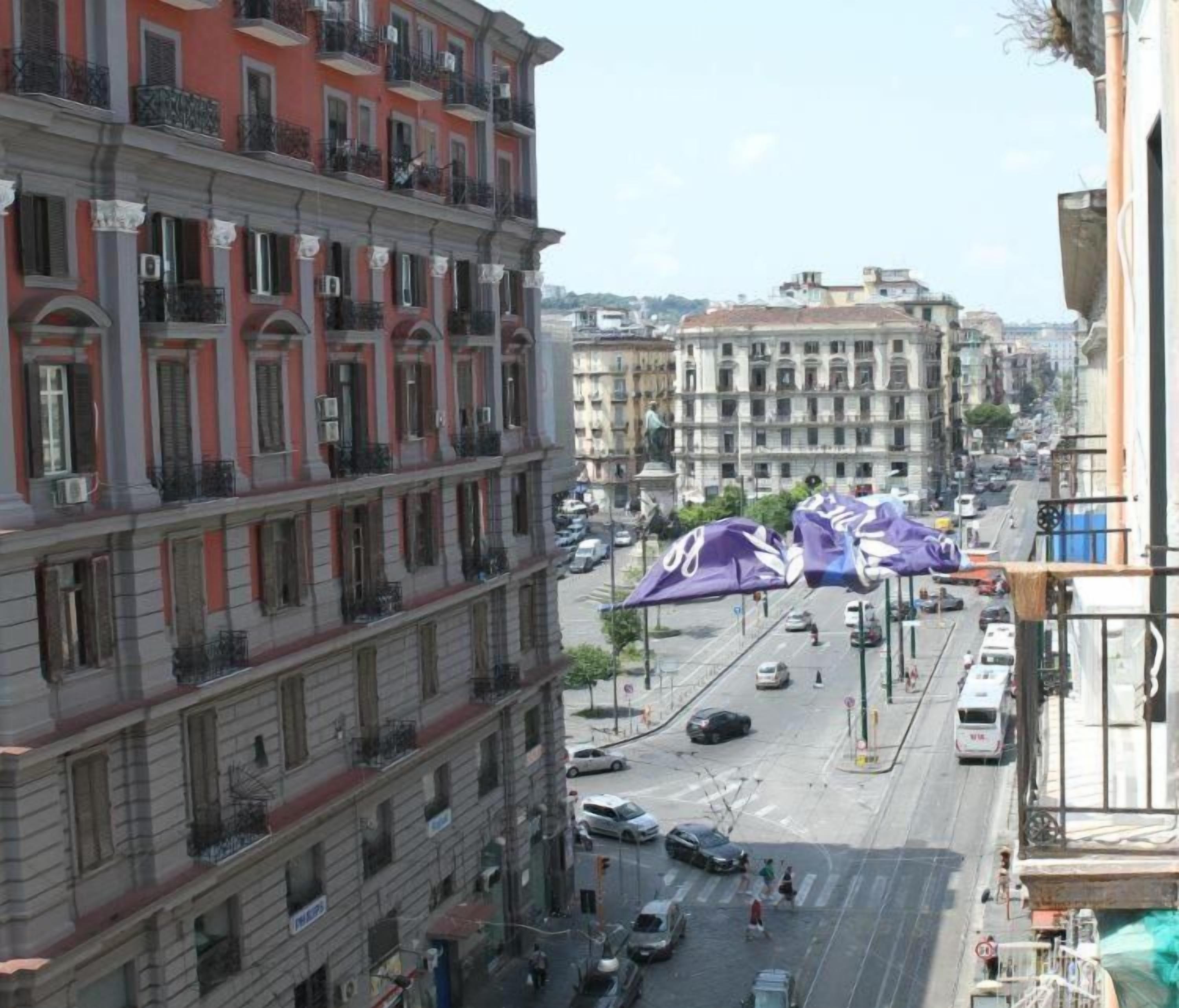 A multi-story building with balconies, a street view, and parked cars.