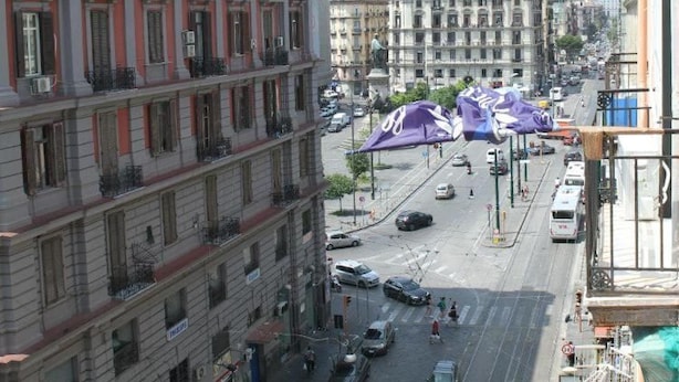Un immeuble à plusieurs étages doté de balcons, donnant sur la rue et avec des voitures garées devant.