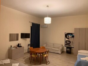 Une pièce comprenant une table à manger, des chaises, un canapé, un lit, un téléviseur et un luminaire au plafond.