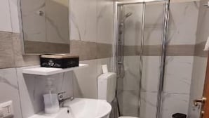 Une salle de bain avec un sol carrelé en marbre, un meuble-lavabo en bois avec un évier, des toilettes et une cabine de douche en verre.