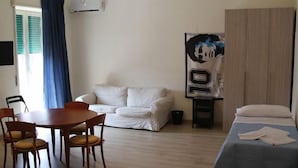 Une pièce comprenant une table à manger, deux chaises, un canapé, un lit et une affiche accrochée au mur.
