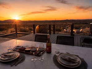 Un montaje para cenar al aire libre con vistas al atardecer, una botella de vino y una comida preparada para dos personas.