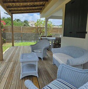 A covered outdoor seating area with wicker furniture and a wooden deck. - Charming beachfront villa, right on the water's edge (La Trinité)