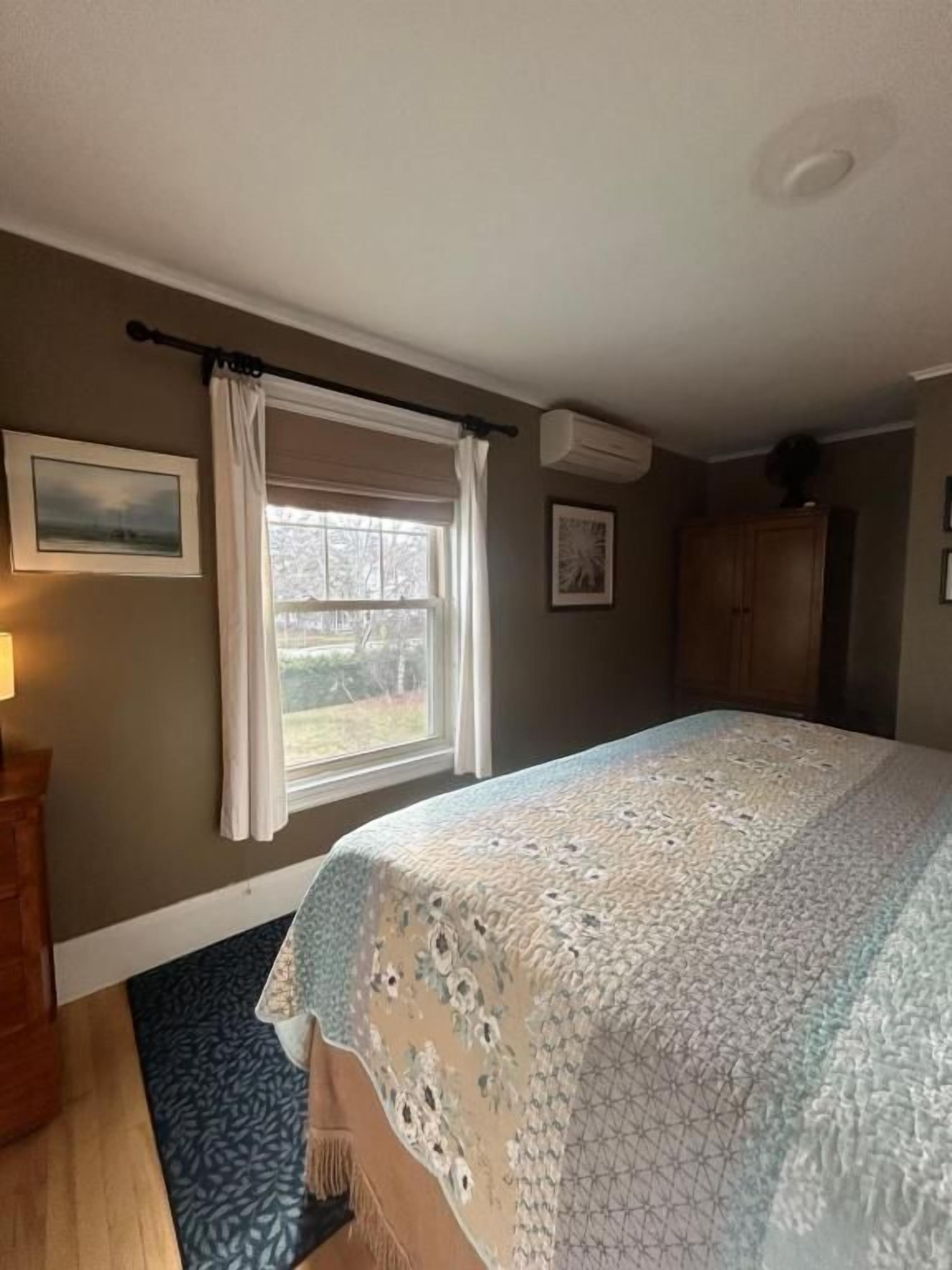 A bedroom with a bed, a window with curtains, a wooden dresser, and a rug.