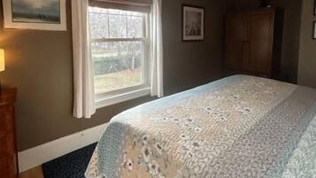 A bedroom with a bed, a window with curtains, a wooden dresser, and a rug.