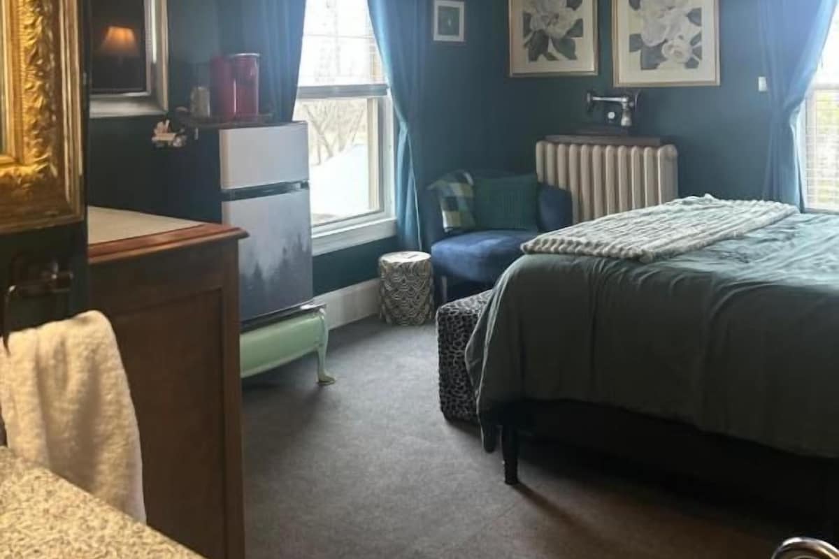 Quarto com cama, cômoda, cadeira, janela com cortinas e radiador.