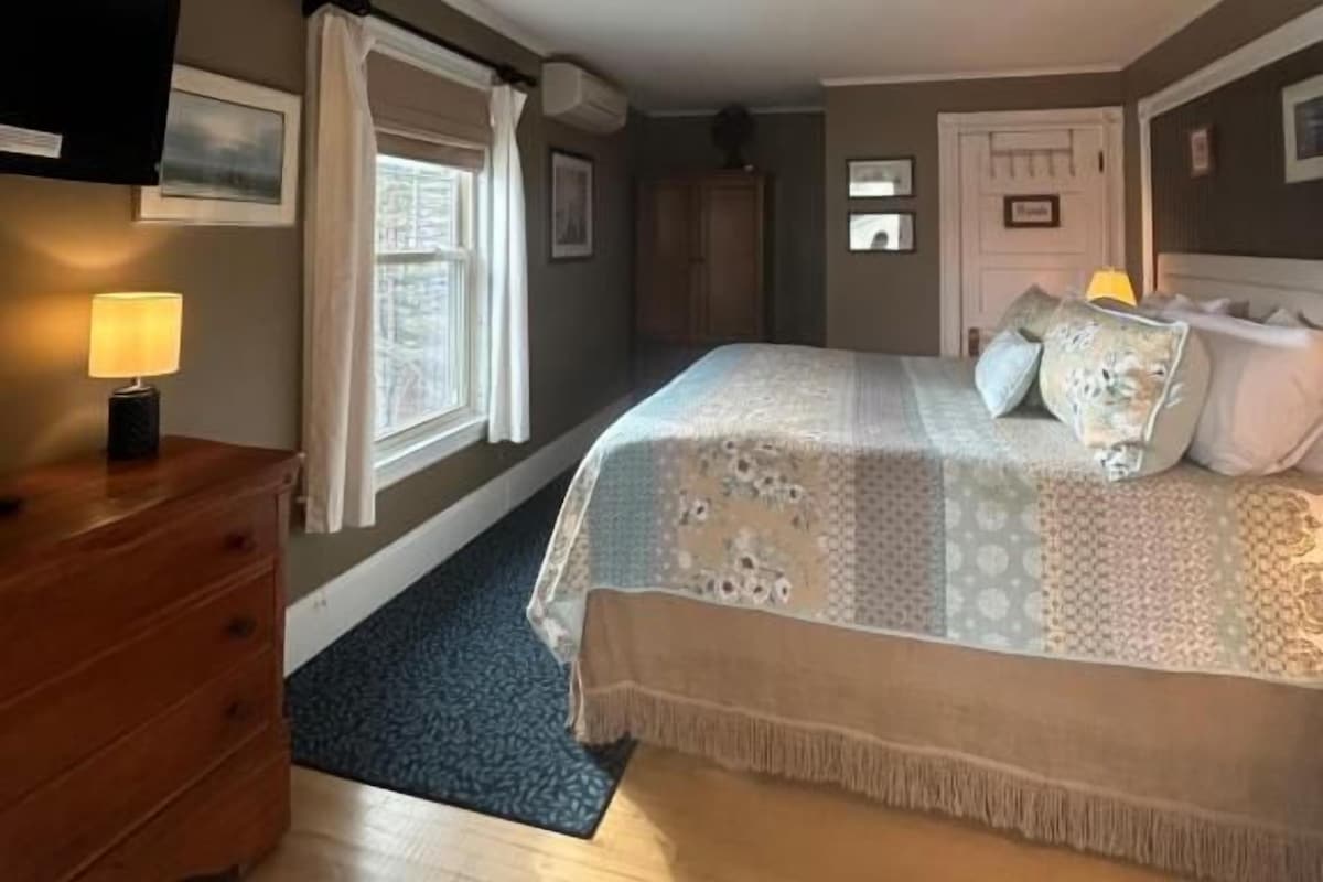 Quarto com cama, penteadeira e janela com cortinas.