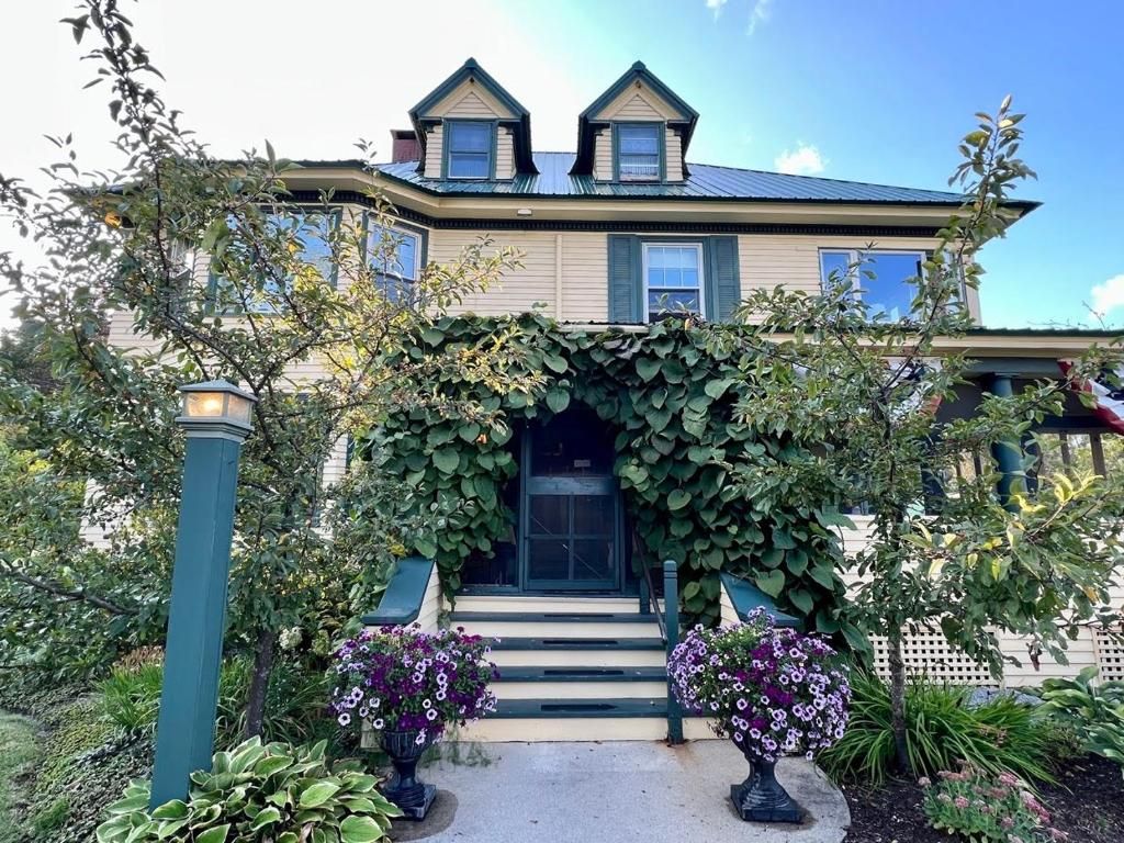 A two-story house with a covered entrance, steps leading up to the door, and potted plants.