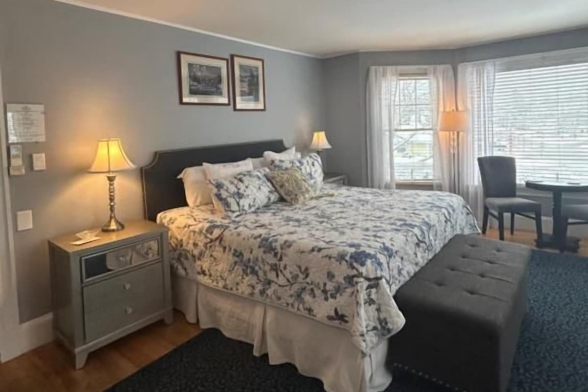 Quarto com cama, mesas de cabeceira, um banco e uma janela.