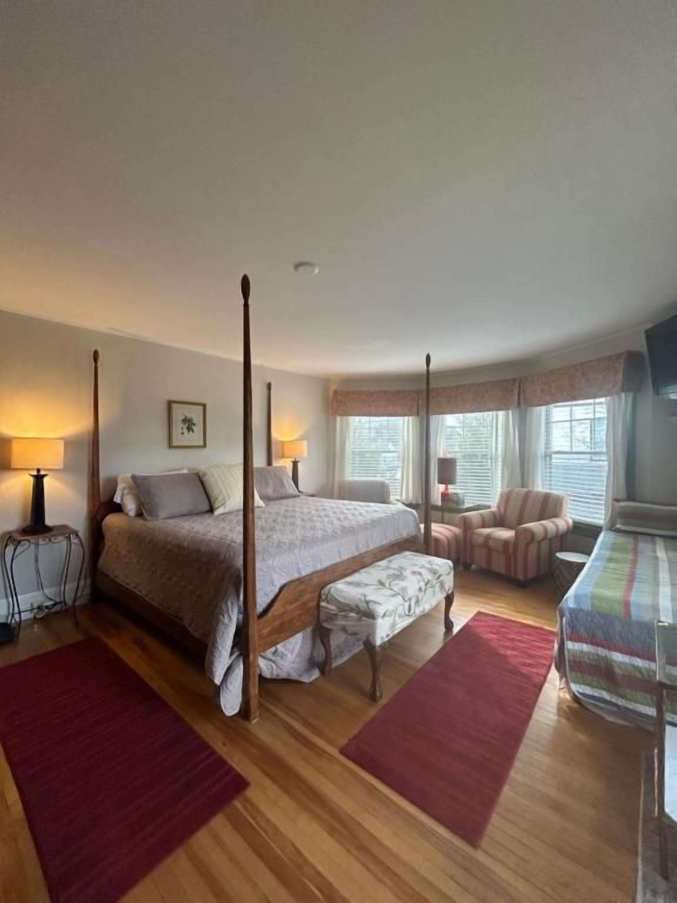 A bedroom with a four-poster bed, a bench, a chair, and a small table.