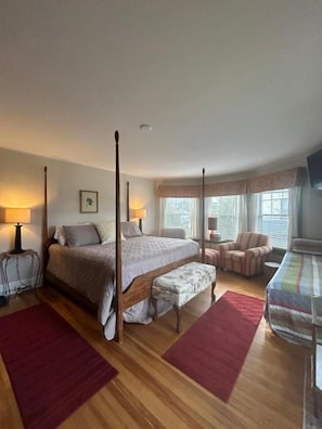 Quarto com cama de dossel, um banco, uma cadeira e uma mesinha.