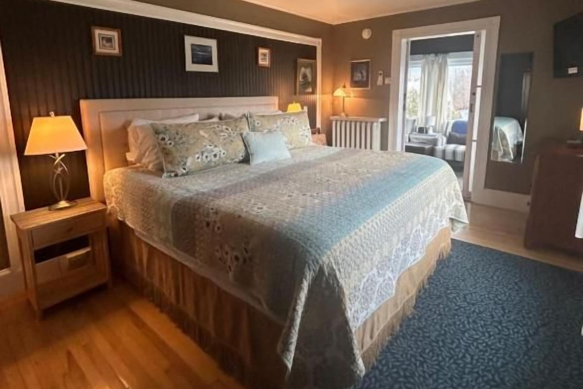 Quarto com uma cama grande, mesas de cabeceira, janela e vista para o exterior.