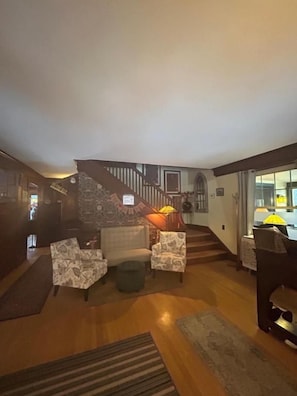 Amplia sala de estar con una escalera que sube a un nivel superior, chimenea y piano.