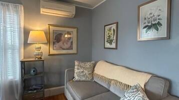 Ein Wohnzimmer mit einer Couch, einer Lampe und gerahmten Kunstwerken an der Wand.