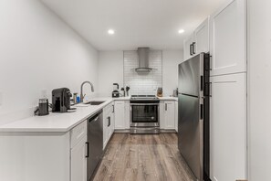 A modern kitchen with white cabinetry, stainless steel appliances, and a wooden floor. - 2 bed, 1 bath Basement Apt. with W/D in Custom Home and 1 Garage Parking Space (Denver)