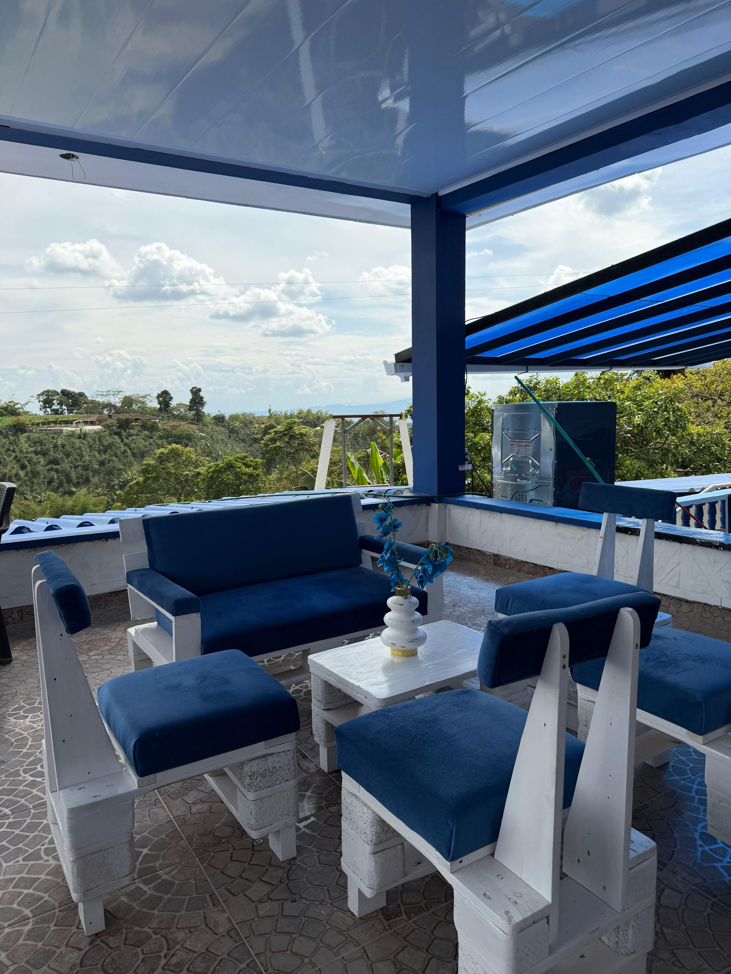 Un'area salotto all'aperto coperta, con mobili imbottiti blu e un tavolo bianco.