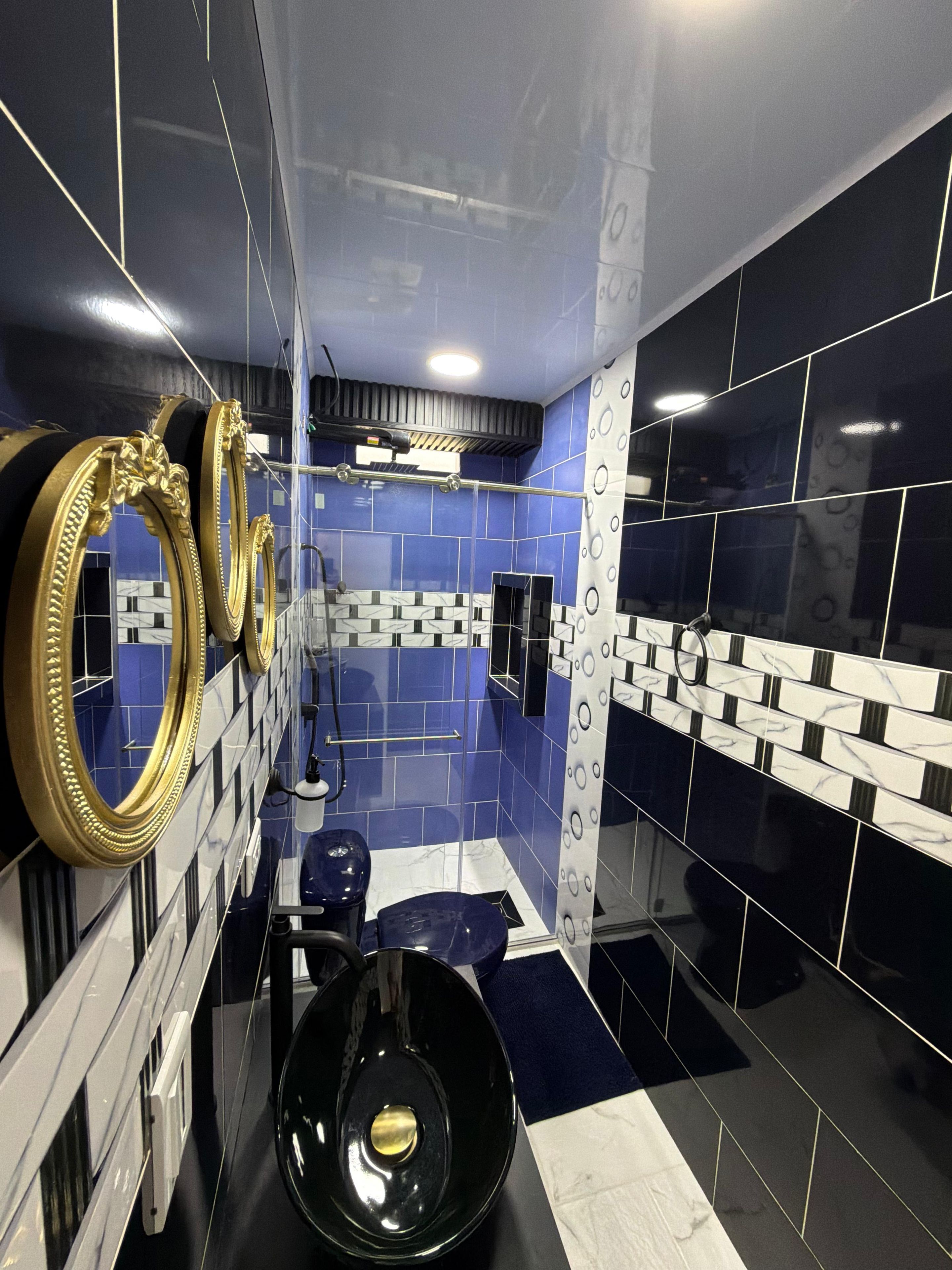 A modern bathroom with blue and black tiles, a gold-framed mirror, and a black toilet.