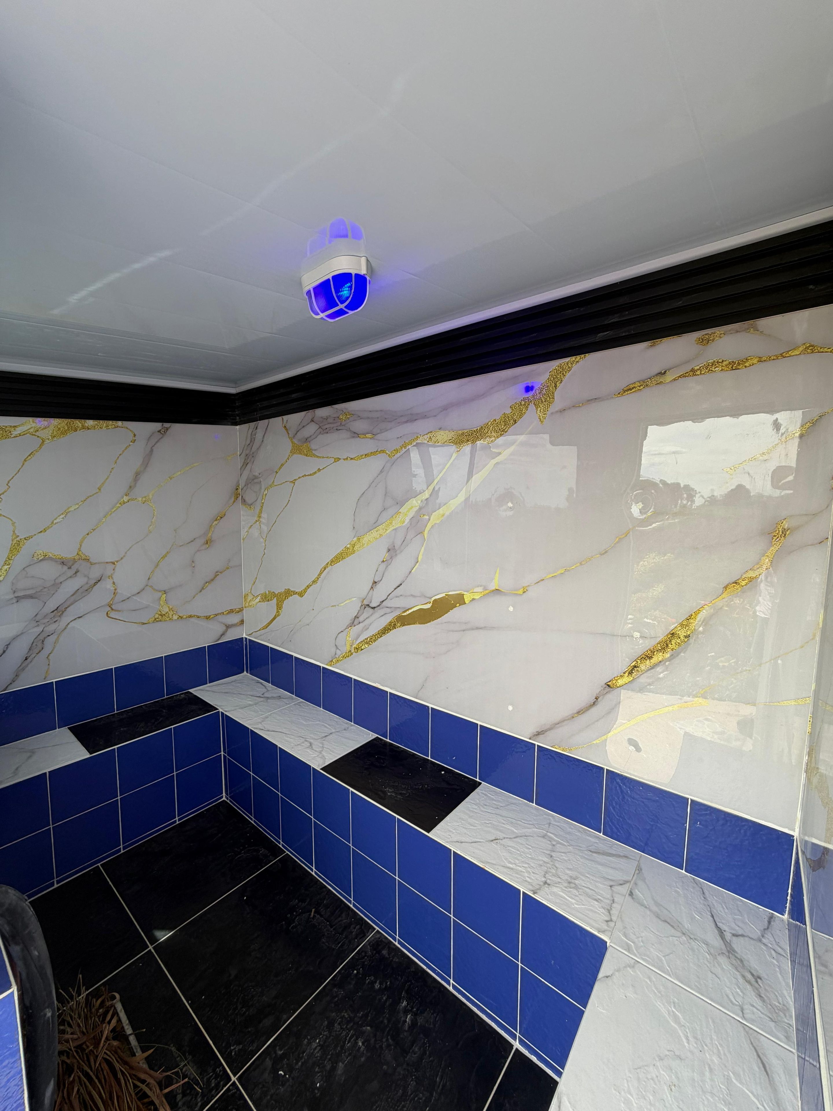 Un baño con pared de mármol blanco, azulejos azules y suelo negro.