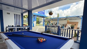 An indoor pool table with a blue felt surface, surrounded by a blue and white color scheme, and a view of the outside through an open door. - Artehotel del Quindío  (Filandia)
