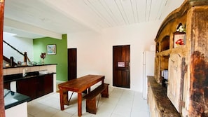 Una stanza con una panca in legno, un tavolo, un angolo cottura con lavello e pensili, e una parete con pannello verde e una porta.