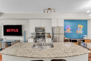 Una cocina moderna con encimera de granito, electrodomésticos de acero inoxidable y un televisor de pantalla plana mostrando 'NETFLIX'.