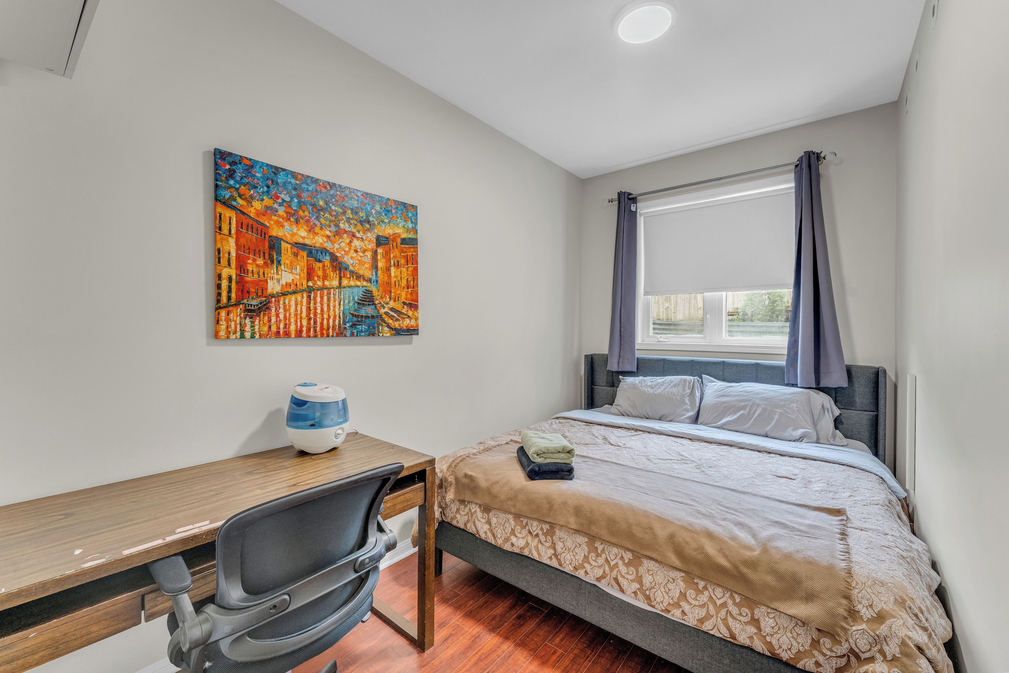 Un dormitorio con cama, escritorio, silla y un cuadro en la pared.