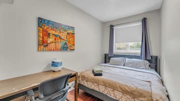 Un dormitorio con cama, escritorio, silla y un cuadro en la pared.