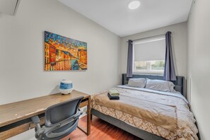 A bedroom with a bed, a desk, a chair, and a painting on the wall. - 2 BR Townhouse with Patio Terrace (Toronto)