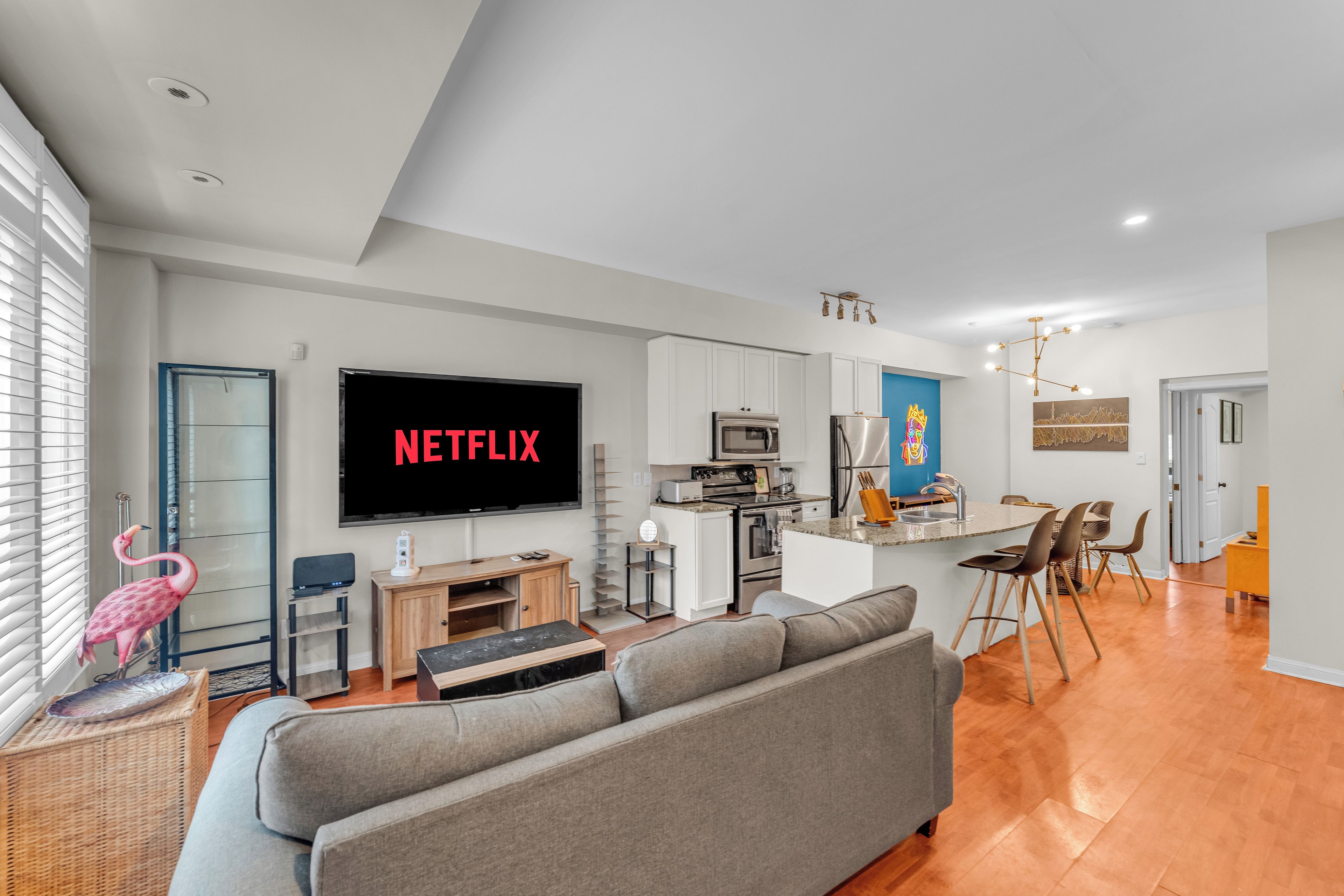 Una sala moderna con un sofá gris, un televisor de pantalla plana y una zona de cocina con armarios blancos y una pared de acento azul.